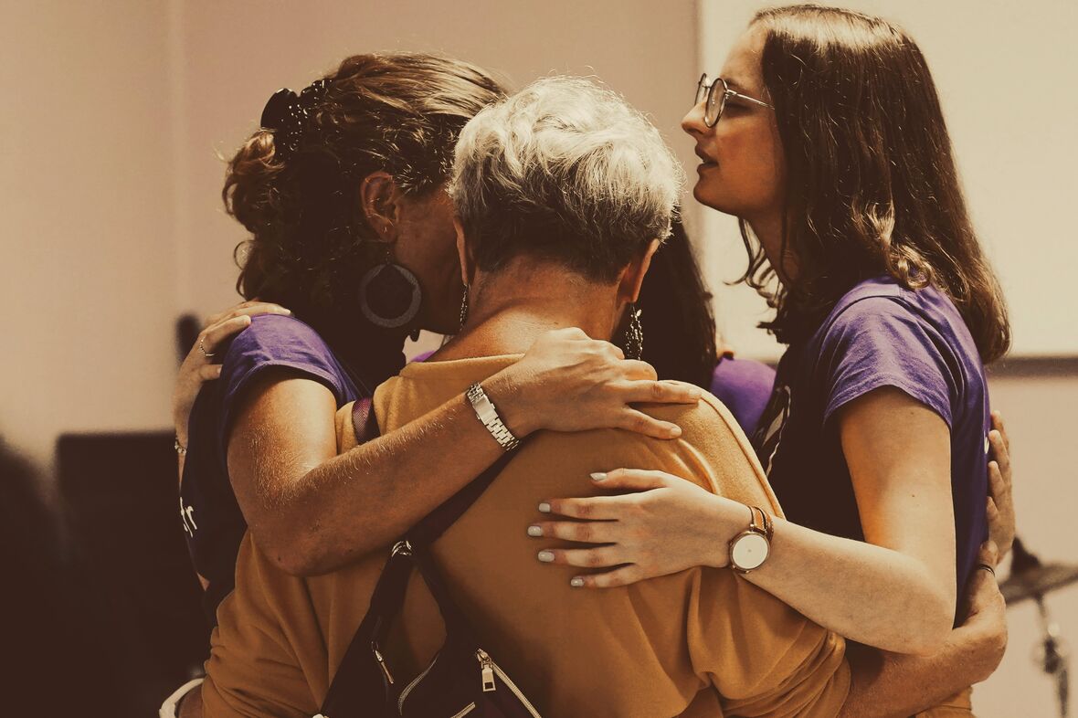An older woman held in a close embrace by two younger women.